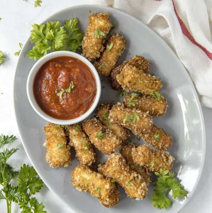 A plated of fried keto mozzarella sticks with a bowl of pizza sauce for dipping.