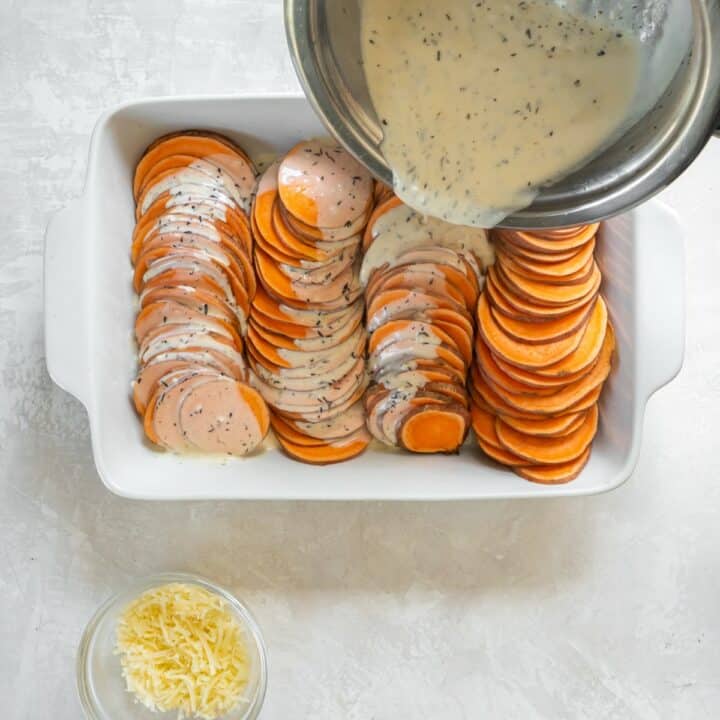 The herb cream cheese sauce being poured over the sweet potato rounds in the baking dish.