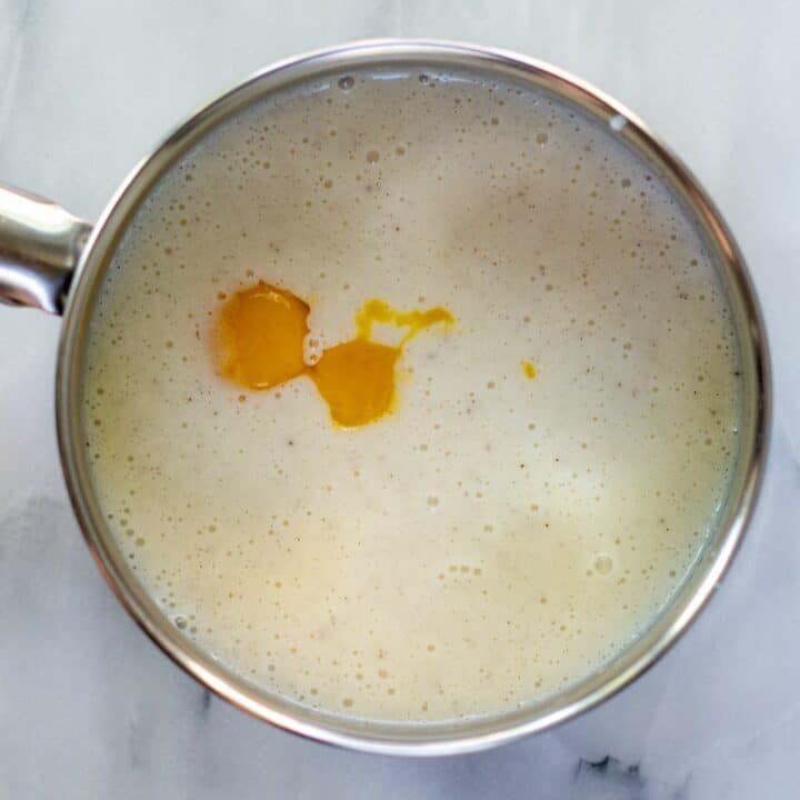 The egg yolks being added to the heated keto pudding mixture in a saucepan.