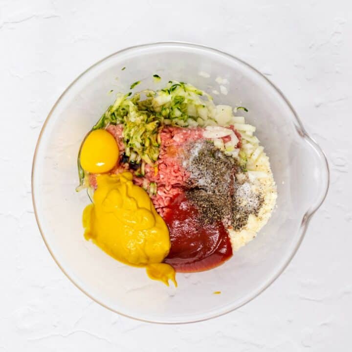 Glass mixing bowl with the unmixed ingredients for making meatloaf.