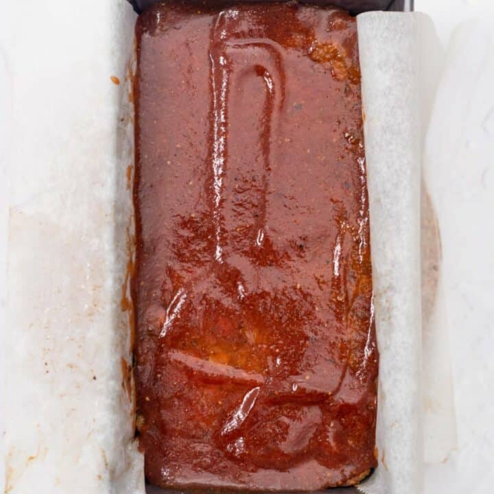 A loaf pan with unbaked meatloaf topped with sugar-free ketchup.