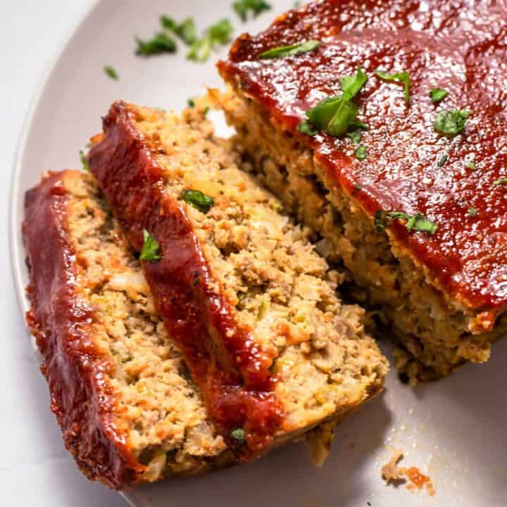 Fully cooked low carb meatloaf on a plate. Two slices have been cut and lay on their side.