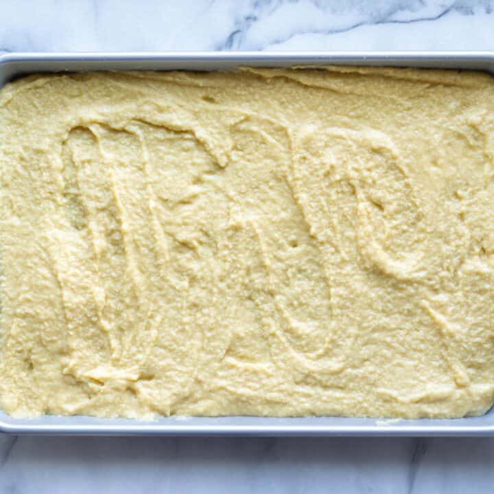 Rimmed baking sheet with stuffing bread batter evenly spread for baking.