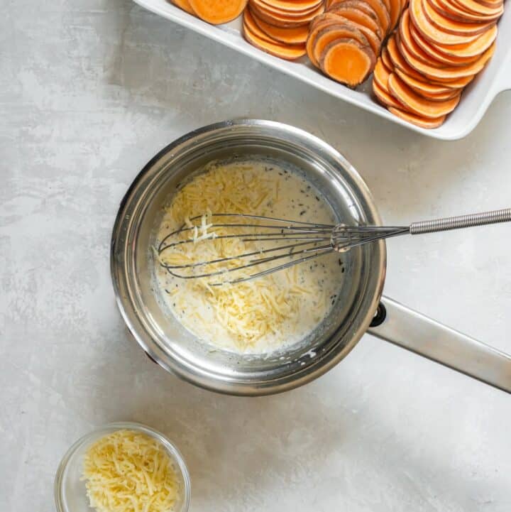 Parmesan and gruyere cheese being whisked into the herb cream sauce in a small saucepan.