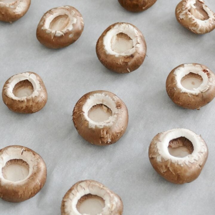 Empty mushroom caps on a parchment lined baking sheet ready to be filled.