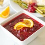 Keto cranberry sauce in a white bowl with an orange slice on top.