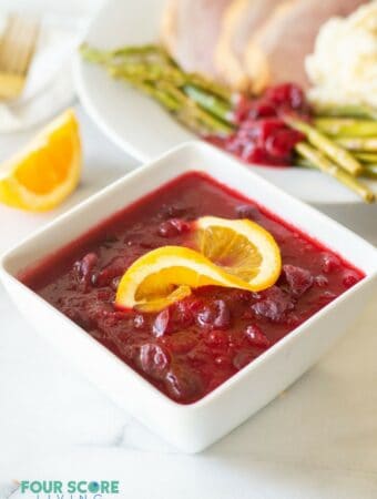 Keto cranberry sauce in a white bowl with an orange slice on top.