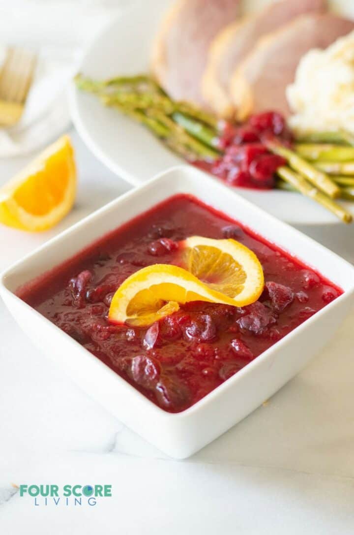 Keto cranberry sauce in a white bowl with an orange slice on top.