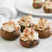 Four keto stuffed mushrooms with cream cheese and bacon on a small square plate.