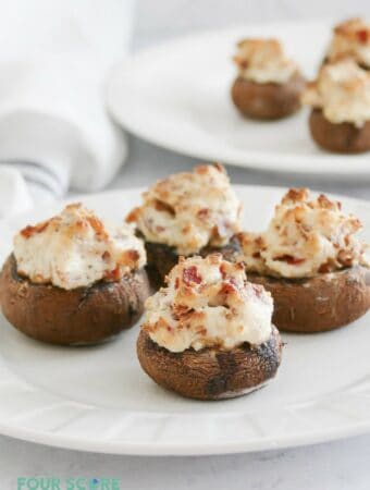 Four keto stuffed mushrooms with cream cheese and bacon on a small square plate.