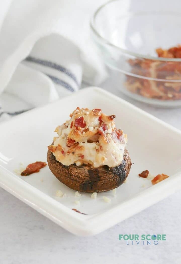 A keto stuffed mushroom with cream cheese and bacon on a small square plate.