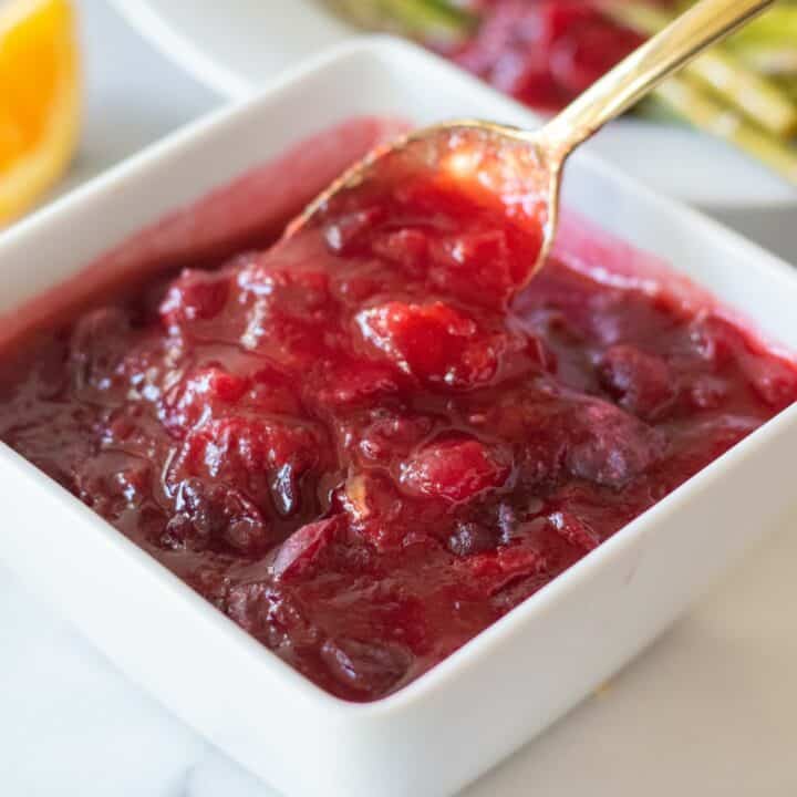 A small spoon is taking a spoonful of keto cranberry sauce from a filled small dish.