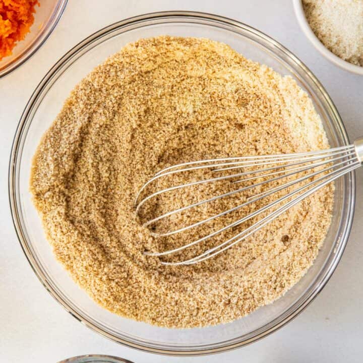 Glass bowl with almond flour, baking soda, salt, cinnamon and nutmeg being whisked together.