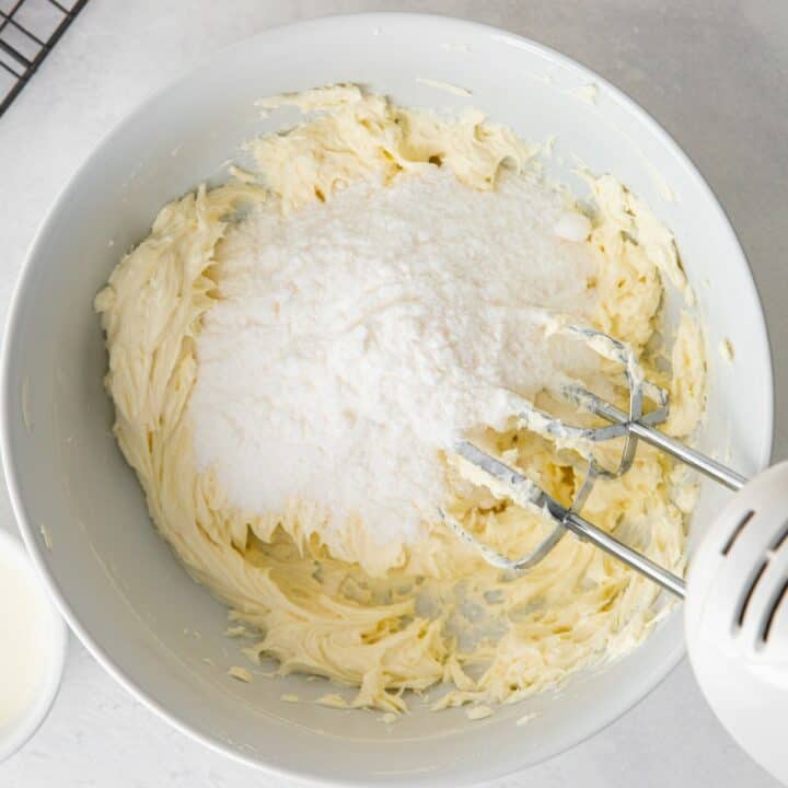 Powdered sweetener being added to the mixed cream cheese and butter. Being mixed together with a hand mixed.