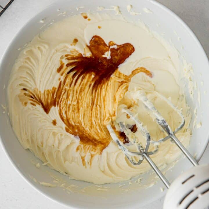 Vanilla and cream being mixed into the keto cream cheese frosting with a hand mixer.