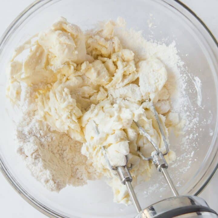 Room temperature cream cheese and powdered sweetener being mixed by a hand mixed.