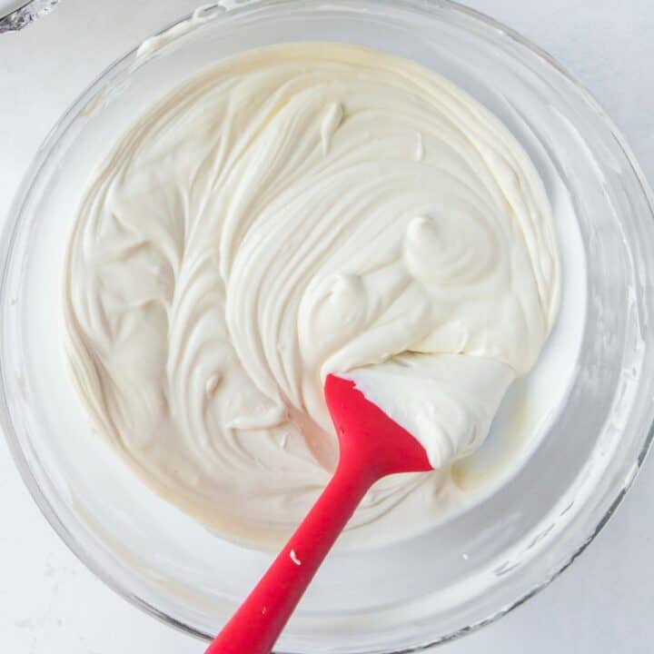 Smooth and creamy cheesecake filling being mixed with a spatula in a glass bowl.