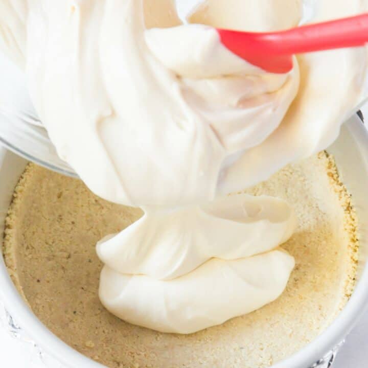 The cheesecake filling being poured onto the baked and cooled crust in a springform pan.