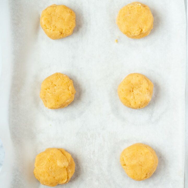 Parchment lined baking sheet with 6 unbaked almond flour biscuits.