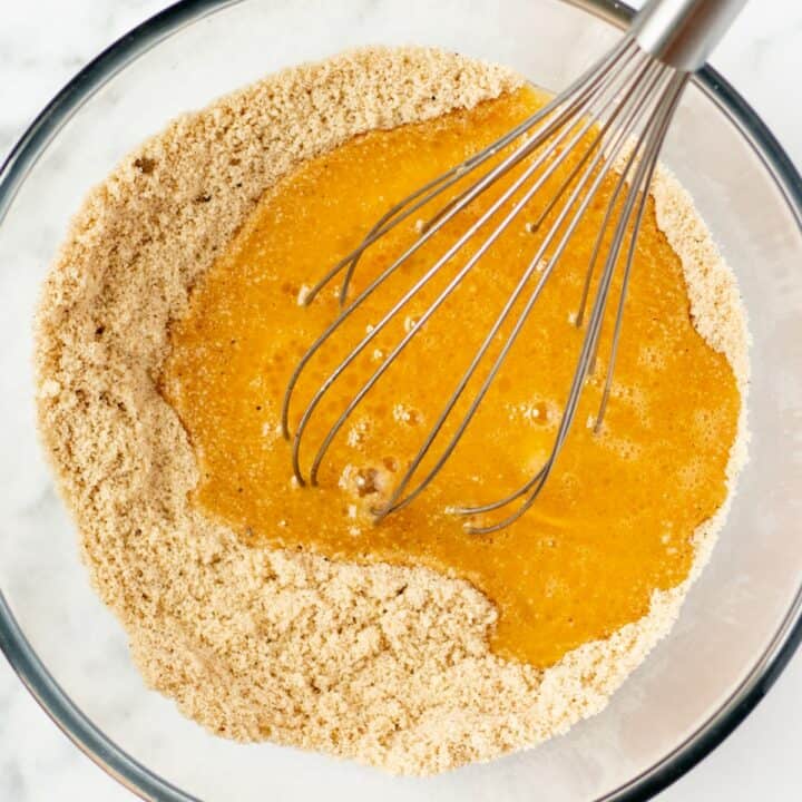 The wet ingredients being mixed into the dry ingredients with a whisk in a glass bowl.