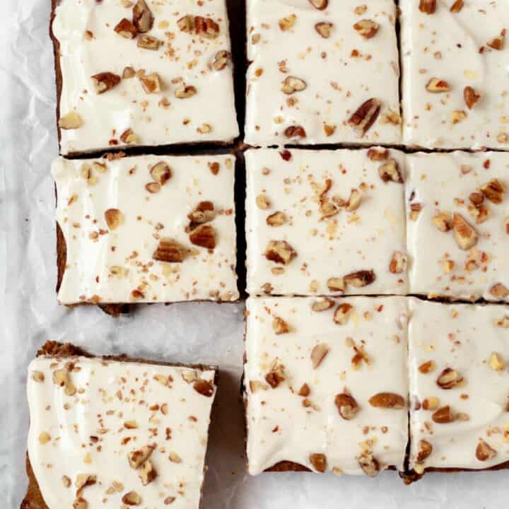 The carrot cake topped with frosting and chopped pecans cut into nine square bars.