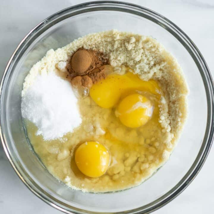 Eggs, oil, sweetener, cinnamon and vanilla extract being added to the flour mixture in a glass bowl.