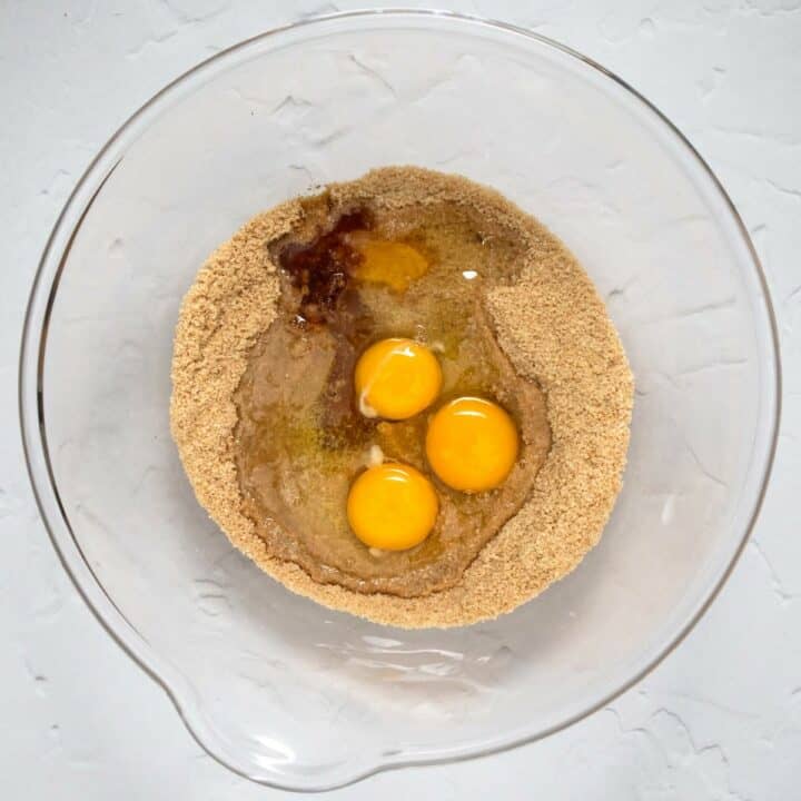 Eggs, oil, syrup and vanilla extract being added to the mixed dry ingredients in a glass bowl.