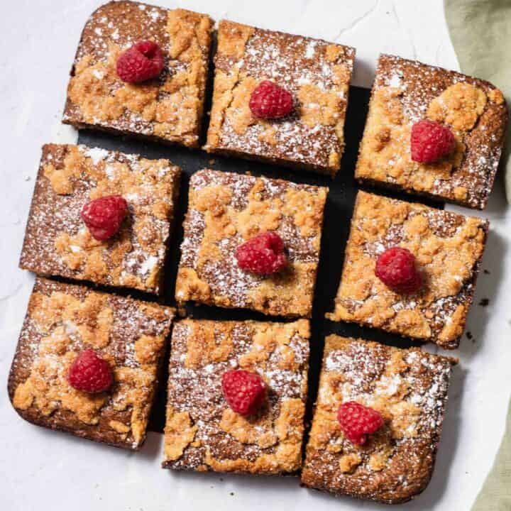 The keto coffee cake removed from the pan and cut into nine square pieces. Each square is topped with a raspberry and a dusting of powdered sugar.