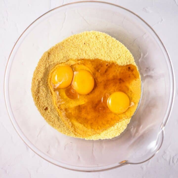 Glass bowl with the wet ingredients being added to the mixed dry ingredients to make the keto cornbread batter.