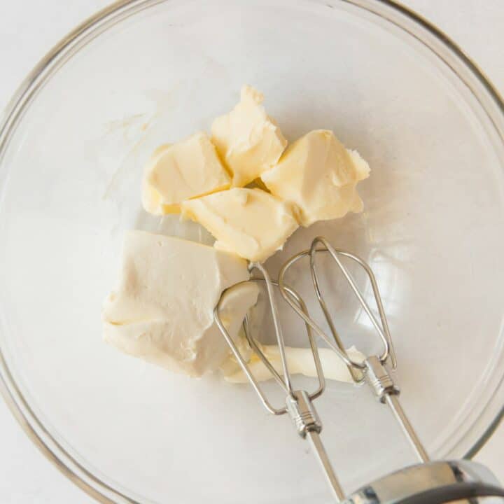 Glass bowl with a hand mixer about to mix the room temperature butter and cream cheese together.