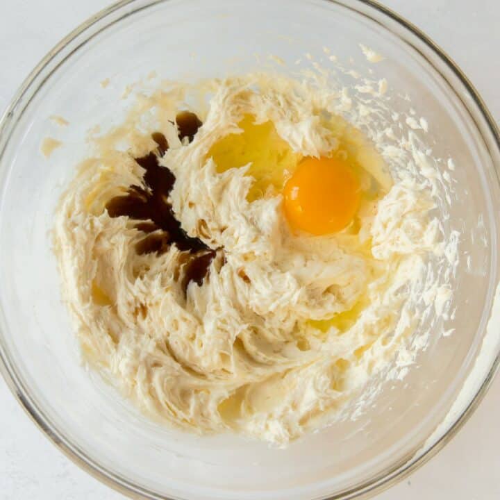 In a glass bowl, the egg and vanilla extract are being added to the butter, cream cheese and sugar mixture.