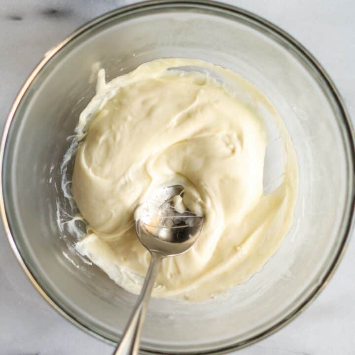 Glass bowl with melted mozzarella and cream cheese being mixed together with a spoon.