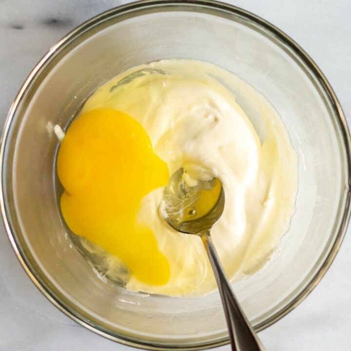 Glass bowl with an egg being mixed into the cheese mixture with a spoon.