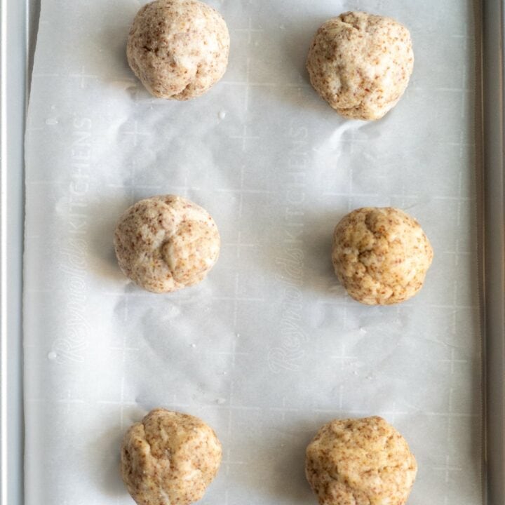 Six balls of dough on a parchment lined baking sheet ready to be baked.