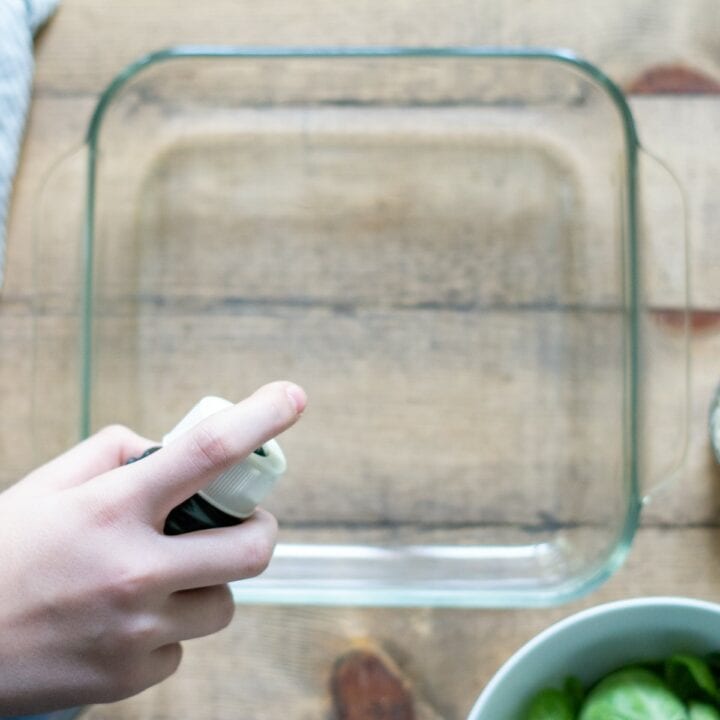 Square glass baking dish being sprayed with oil.