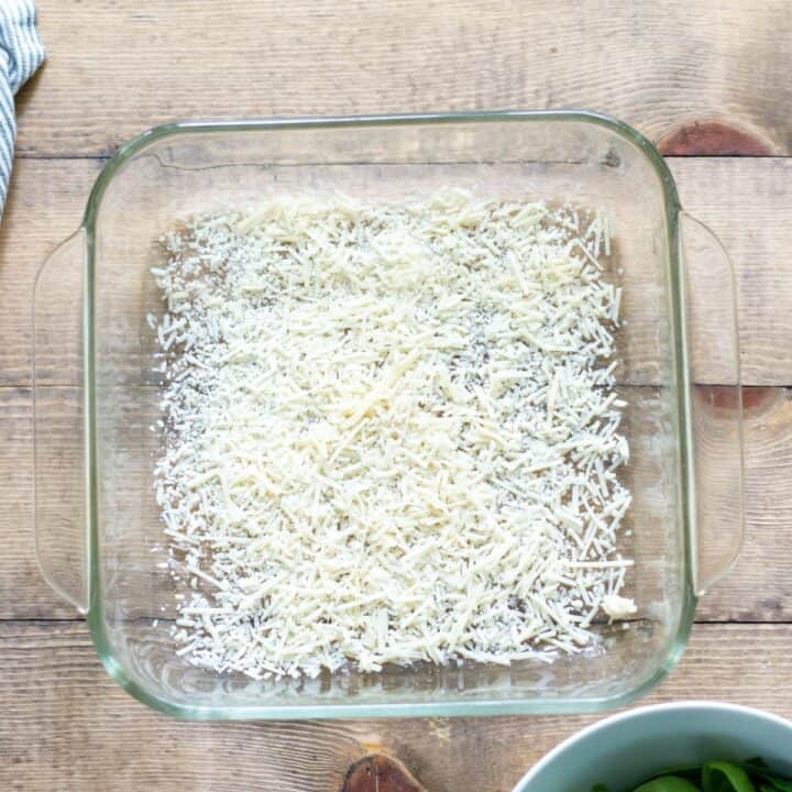 Freshly grated parmesan cheese sprinkled evenly over the bottom of a square glass baking dish.