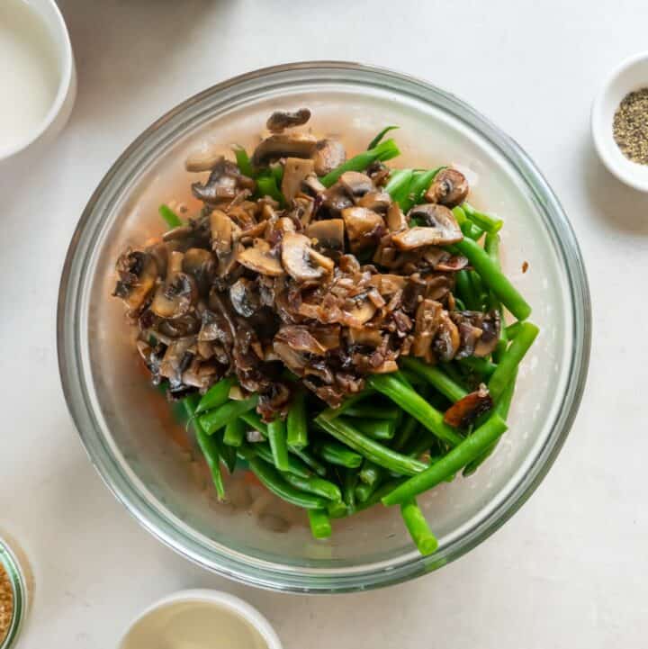 A glass bowl filled with the blanched green beans and cooked mushrooms, garlic and onions.