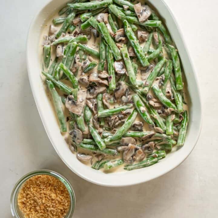 A casserole dish filled with the green bean casserole mixture next to a bowl of crushed pork rinds.