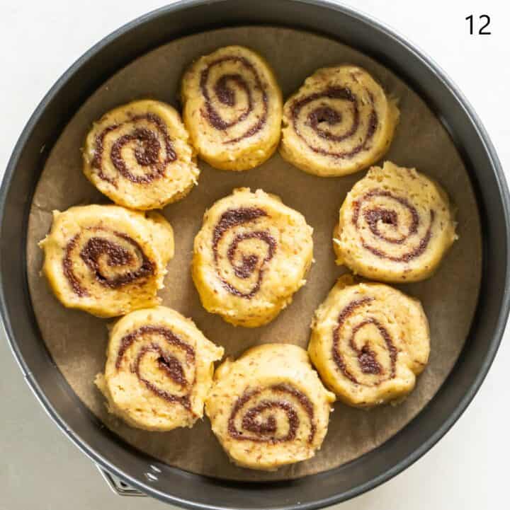 Nine cut cinnamon rolls in a parchment lined cake pan.