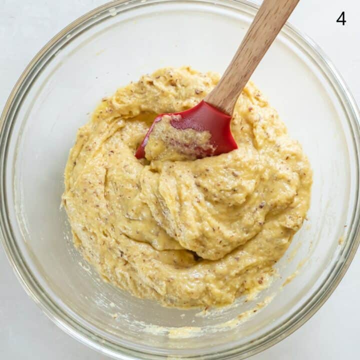 The wet and dry ingredients being mixed together with a spatula in a glass bowl.