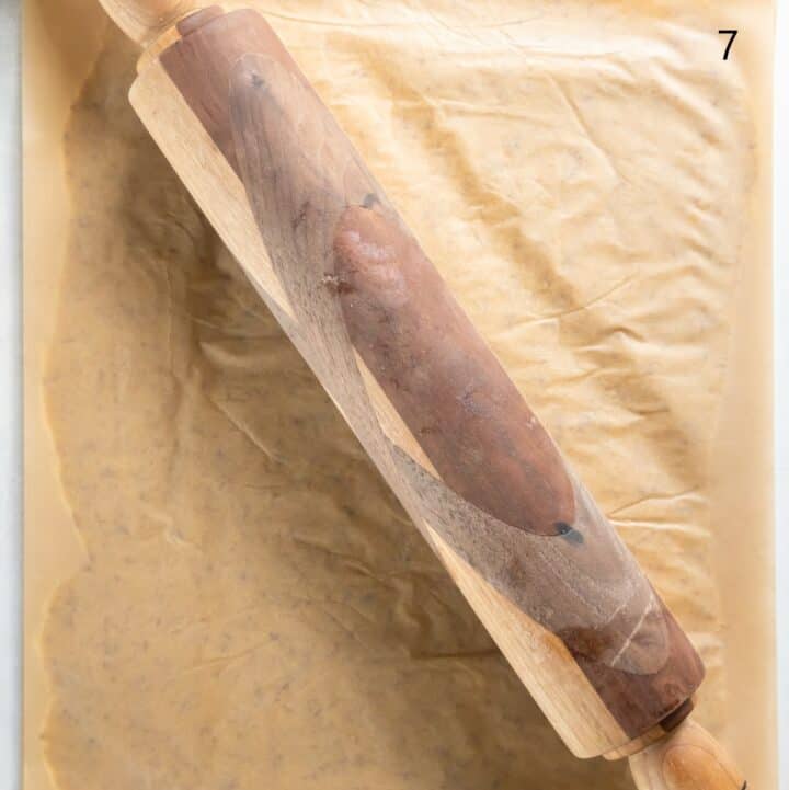 A rolling pin rolling the dough between two layers of parchment paper.