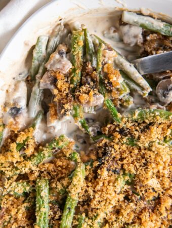 A spoonful of keto green bean casserole being scooped out of a casserole dish.