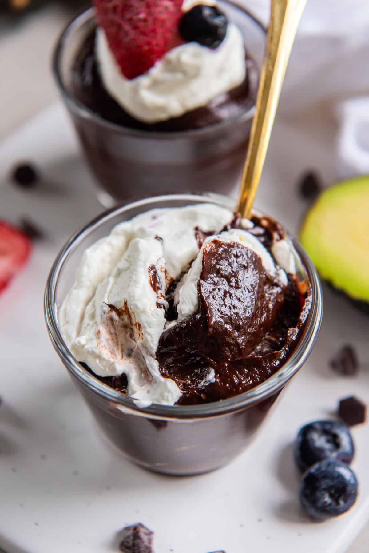 A spoonful of avocado chocolate pudding and whipped cream topping being taken from a small dessert glass.