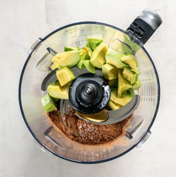 Food processor with avocado chunks, cocoa powder, maple syrup, salt and vanilla extract.