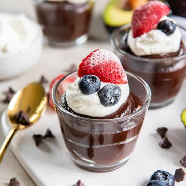 Small glass filled with avocado pudding. Topped with whipped cream, 2 blueberries and half a strawberry.