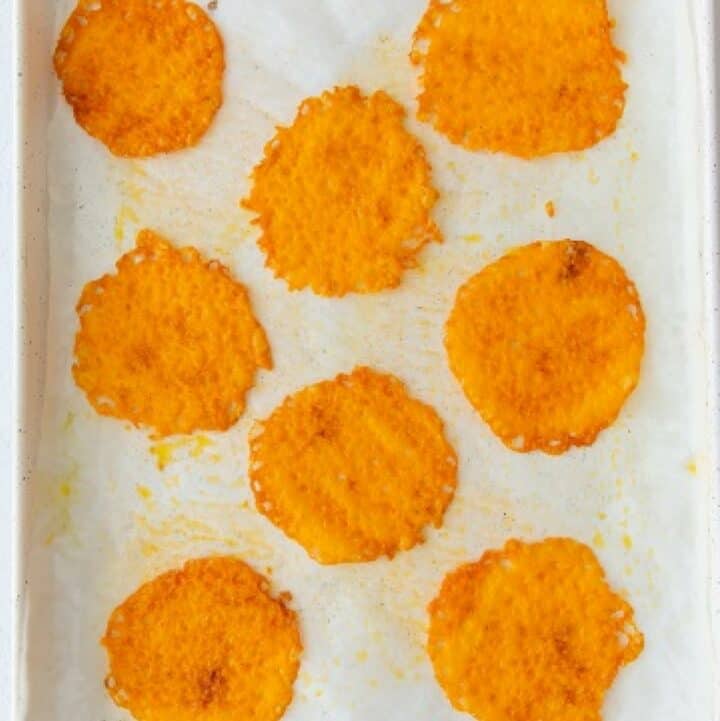 Eight fully baked keto cheese chips on a parchment lined baking sheet.