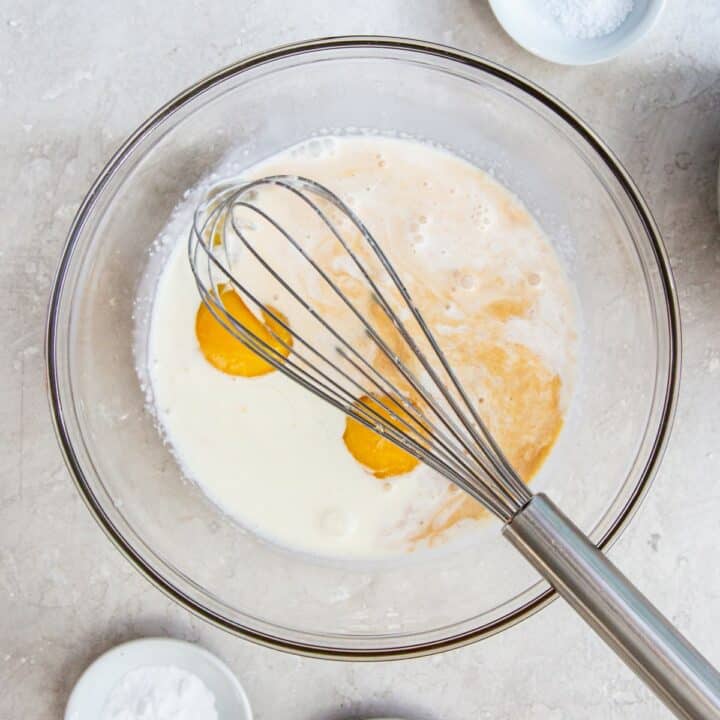 Heavy cream, water, sweetener, vanilla extract and eggs being whisked together in a glass bowl.