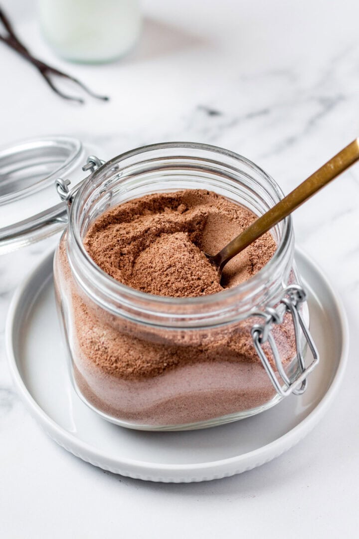 A spoonful of keto hot chocolate mix being scooped out of a glass jar with airtight clamp lid.