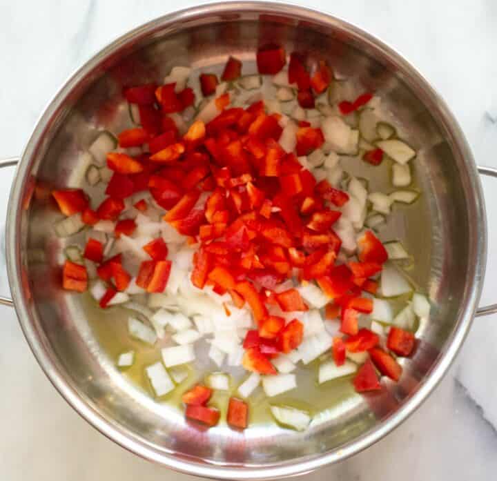 Large pot with diced onions and bell peppers cooking in oil.