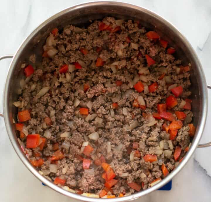 A large pot with cooked beef, onions and bell peppers.